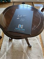 Photo showing top view of the round wooden occasional table with a dark finish and subtle edge detail, along with a paper indicating lot number.