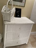 Photo of white rattan dresser with three drawers and the magazine holder basket placed on top, showing condition and overall appearance.
