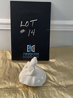 Photo of the pure white Royal Doulton ballerina figurine seated on skirt with a black backdrop showing lot number