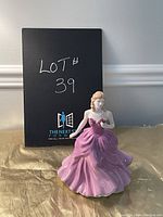 Full view of the Royal Doulton figurine in front of a black sign marked 'LOT 39'. The figure is shown in a front pose highlighting the flowing pink gown and detail of the flower in hand.