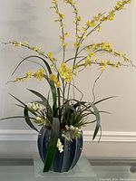 Front view of blue ridge-detailed vase holding yellow faux flower arrangement with green leaves