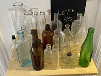 Front view of the collection of 20 glass bottles in various colors and shapes on wooden tray