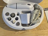 Full view of vintage Homemedics electric manicure set, with device, six heads, power adapter, and coiled cord in white plastic case.