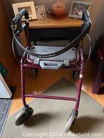 View of the front of the Dolomite folding walker showing the brand name on the crossbar and the padded handles with brakes.