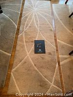 Full length view of cream wool runner rug with visible starburst pattern embossed at center and curved lines along its length on wooden floor.