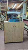 Full front view of Delta random orbital bench sander on wooden cabinet stand with firewood stacked in background.