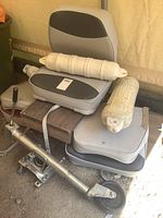 Photo showing 3 strap on folding boat seats stacked, two small and one large white boat bumpers resting on seats, and trailer jack on floor.