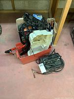 Full lot overview showing battery booster pack with jumper cables, Motomaster battery charger, solar trickle charger, cables and a red battery box with white insert.