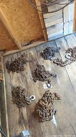 Five rusty metal chains laid on a wood floor inside a shed, each with metal hooks at both ends, varying sizes clearly visible