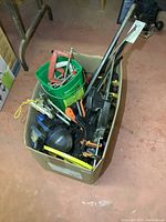 Box filled with various clamps including quick clamps with black and orange handles, visible metal pry bar and green container with smaller clamps