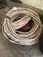 Coils of white, red, and black covered electrical wire arranged on ground