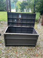 Open resin deck box on ground with lid lifted, showing interior and external panel design.