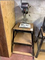 Full view of Delta 8 bench top drill press mounted on wheeled wooden and metal stand with manual on top.