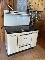Front view of white enamel stove with black cast iron cooktop, oven doors and back shelf