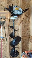 Full view of ice auger hanging in shed, showing engine housing, frame handles and full length auger bit