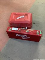Two red Milwaukee cases stacked on floor: metal reciprocating saw case and plastic circular saw case