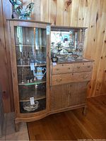 Front view showing curved glass display door, drawer section, lower doors and mirrored back