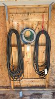 Three coils hanging on shed wall (two black cords, multi-color wire) plus red rope and chain on floor