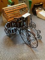 Front and side view of the tricycle-shaped plant stand showing metal scrollwork wheels and two pot holders with wood slats.