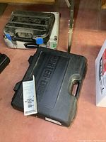 Closed black plastic Porter-Cable case and two silver aluminum cases on floor.