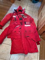Two red Snow Goose jackets laid flat on tile and wood floor