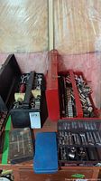 Two metal tool boxes, one black and one red, filled with assorted sockets and a few small storage boxes in front.