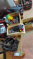Photo showing two Jobmate tool bags with open tops displaying a variety of hand tools such as cutters, screwdrivers with colorful handles, wrenches, pliers, and a hammer scattered on table around boxes.