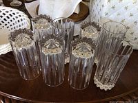 Photo showing 8 tall heavy cut crystal glass drinking glasses with vertical and starburst cut pattern, displayed on table surface.