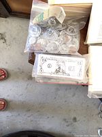 Image showing a ziplock bag containing many plastic play coins and a separate ziplock bag with paper play money bills including a one-dollar bill with cartoon design.