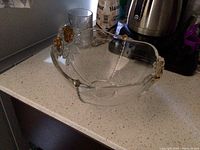 Photo of the clear glass serving bowl with gold floral design on the rim placed on kitchen counter next to other items.
