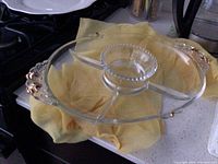 Glass serving dish with a central dip bowl and gold painted floral accents on the handles, placed on a kitchen counter.