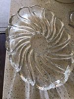Photo showing clear glass oval serving dish with detailed swirling rib pattern on a speckled countertop.