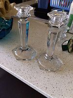 Pair of clear glass candlesticks displayed on a speckled countertop.