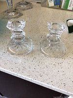 Photo of two short clear glass candlesticks with multi-faceted stems and octagonal bases on a countertop.