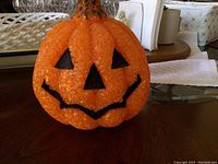 Orange plastic pumpkin shaped Halloween decoration with a smiling jack-o'-lantern face, placed on a glass table.