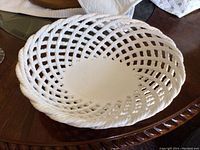 White opaque glass braided serving bowl with open lattice spiral design, placed on wooden surface.