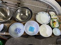Kitchen bowls and strainers displayed on a bench with oven mitts and small utensils visible