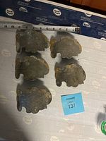 Five small leaf-shaped brass plates arranged together on a surface with a measuring tape showing size around 3-4 inches wide. Plates show tarnish and dark patina.