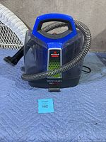 Front view of Bissell SpotClean ProHeat carpet cleaner with attached hose and nozzle sitting on padded surface.