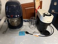 Smeg coffee maker and Nespresso espresso machine side by side on a table with power cords visible.