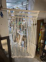 Full view of the cream crochet doorway hanging separator with vertical strips and some wooden beads, hanging on a rod in a cluttered background.