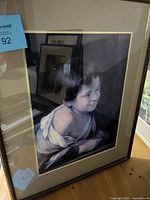 Framed full-color portrait of a young person with short dark hair wearing a white draped garment, visible in the frame and protective glass.