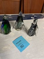 Three glass penguin figurines arranged together on a table with wooden background.