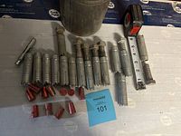View of multiple metal anchor bolts with red inserts, metal canister, measuring tape for scale.