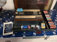 Overhead view of console seated in open storage case with game cartridges, manual and overlays.