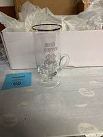 One Irish coffee glass mug with gold rim and shamrock decoration shown outside its box on a table.