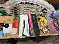 Overview of the lot showing nail dryer lamp, curling wands, flat irons, some packaged and some unpackaged items on a cage style shelf.