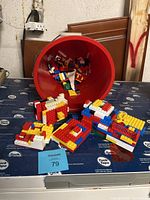 Red bucket tipped with many LEGO pieces spilling out, partially assembled LEGO bricks in front.
