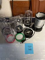 All Magic Bullet components laid out on table including blender base, blending cups, blade assemblies, color-coded sealing rings.