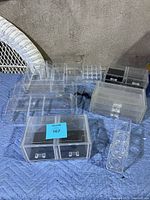 Photo showing the full set of clear acrylic makeup organizers placed on a quilted blue surface, including trays, drawer boxes, and compartment holders.